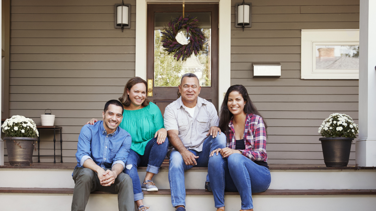 Parents With Adult Children Sitting On Steps in Front Of House